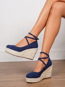 Detalle de sandalias de cuña en ante azul marino con plataforma de cuerda y correas.