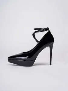 Primer plano de zapatos de tacón de aguja en charol negro con plataforma y correa.