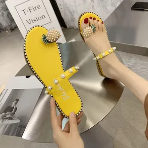 Detailed view of yellow flat thong sandals featuring pearl pineapple and studded straps.