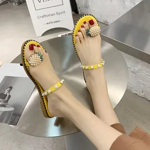 Close-up of yellow flat thong sandals with elegant pearl straps and pineapple charm