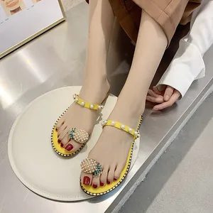 Detail view of yellow flat sandals with pearl pineapple embellishment on foot