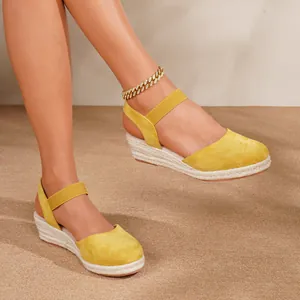 Sandalias de cuña tipo esparto amarillas con puntera cerrada y correa al tobillo.