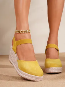 Primer plano de sandalias de cuña amarillas con suela de yute y correas.