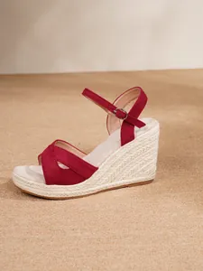 Side view of red suede wedge sandals with braided straw platform and ankle strap.