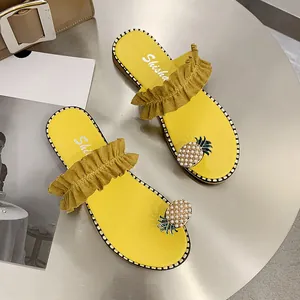 Close-up of yellow fashion flat sandals with ruffle straps and pearl pineapple decor.