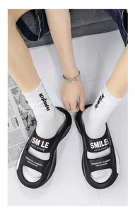 Close-up of black EVA slides with 'SMILE' text worn with white socks on a white floor