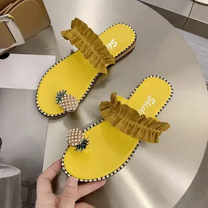 Detailed view of yellow flat sandals featuring ruffled straps and pearl pineapple decor.