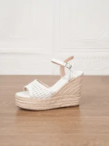 Detalle de sandalias de cuña blancas con plataforma de esparto y tira ajustable al tobillo.