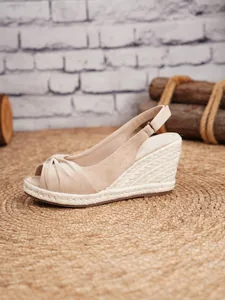 Primer plano de sandalia de cuña de ante beige con nudo y correa trasera ajustable.