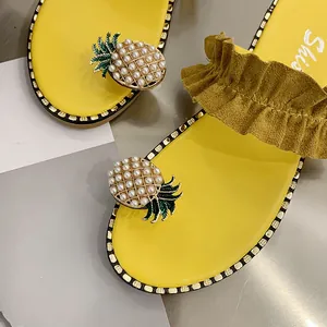 Close-up of yellow flat sandals with pearl pineapple decoration and ruffled strap