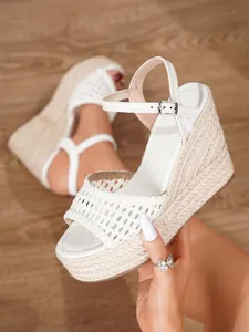 Primer plano de sandalias de cuña blancas con tira trenzada y plataforma de esparto.