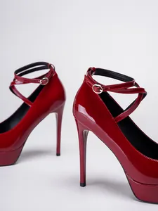 Detalle de tacones de charol rojo con tacón de aguja y correas cruzadas al tobillo.