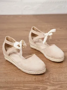 Vista lateral de sandalias de cuña tipo alpargata de lona beige para mujer con cintas.