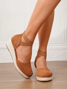Detalle de sandalias de cuña de ante marrón con tiras elásticas cruzadas en los pies