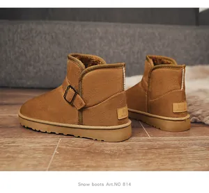 Close-up of brown suede snow boots with buckle and warm plush lining on wooden floor