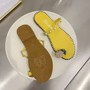 Yellow flat sandals with pearl straps and pineapple charm on a white display tray