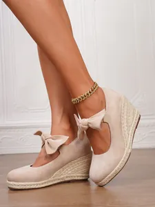 Primer plano de sandalias de cuña de ante beige con lazo y suela de esparto.