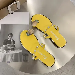 Detail view of yellow flat sandals featuring pearl straps and pineapple decor.