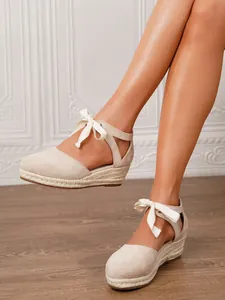 Detalle de sandalias con cuña de lona beige con suela de yute y lazo en el tobillo