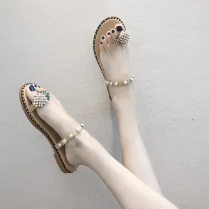 Close-up of women's beige flat thong sandals featuring a decorative pearl pineapple charm