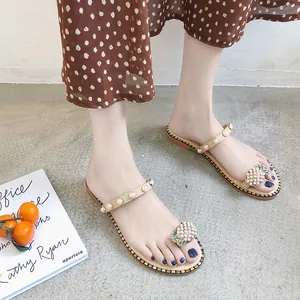 Close-up of women's flat sandals with pearl straps and pineapple charm on model's feet