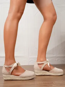 Vista lateral de elegantes alpargatas con cuña beige con un lazo y suela de esparto