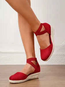 Primer plano de alpargatas con cuña de ante rojo y elegantes correas cruzadas al tobillo.