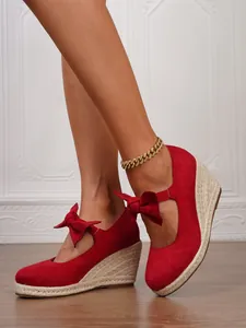 Primer plano de sandalias de cuña de ante rojo con un detalle de lazo muy decorativo.