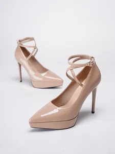 Vista detallada de elegantes tacones de aguja con plataforma en charol beige y tiras cruzadas.