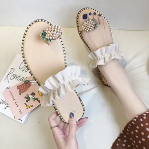 Detailed view of flat thong sandals with ruffled strap and pearl pineapple ornament.
