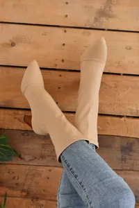 Detailansicht beigefarbener Stretch-Stiefeletten mit Blockabsatz auf Holzgrund