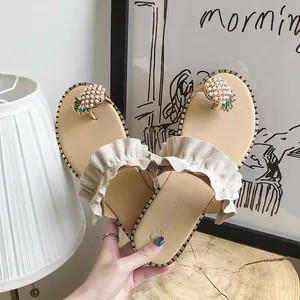 Detail view of beige flat thong sandals with ruffled straps and pearl pineapple decor