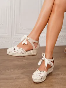 Primer plano de alpargatas de cuña de ganchillo beige con cintas sobre suelo de madera.