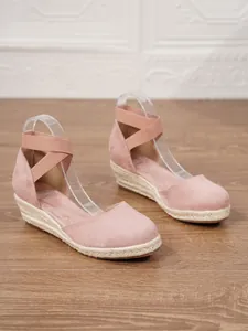 Primer plano de sandalias de cuña en ante rosa con ribete de cuerda de alpargata y correas