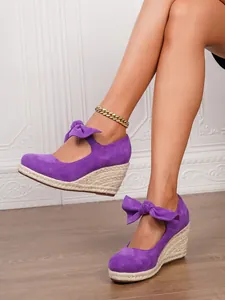 Elegantes sandalias de cuña en gamuza morada con plataforma de esparto y lazos en los tobillos.
