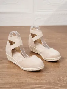 Vista detallada de las elegantes sandalias de cuña beige para mujer en suelo madera.