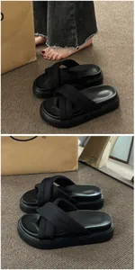 Close-up of black platform sandals with wide crossover fabric straps on a textured rug