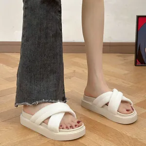 Close-up of women's white platform slippers with ribbed cross straps on wood floor.