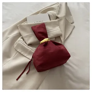 Close-up of a burgundy suede drawstring bucket bag featuring a gold ring handle