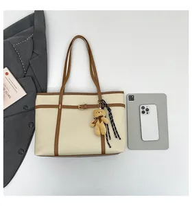 Close-up of beige pebbled leather tote bag with brown trim and bear charm accessory