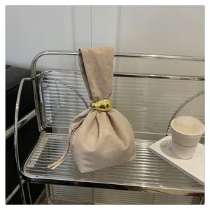 Minimalist beige suede bucket bag with stylish gold ring handle and pleats on acrylic stand.