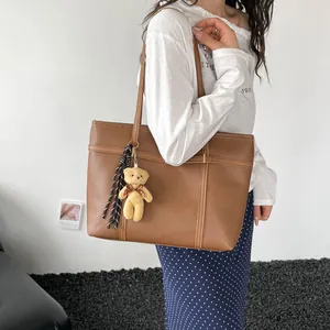 Detail view of a brown minimalist textured tote bag with a cute teddy bear charm on model