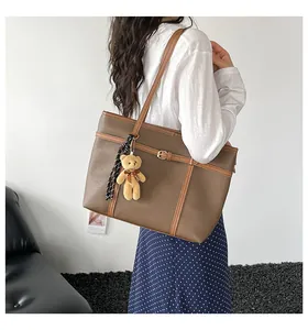 Detailed side view of a woman carrying a brown leather tote bag with a bear pendant
