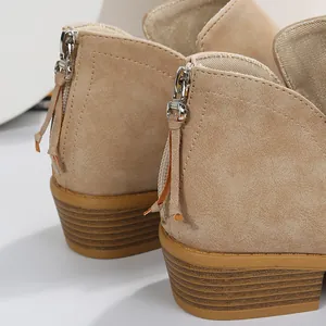 Detail van beige suède enkellaars met ritssluiting aan de achterkant en blokhak