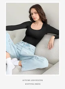 Professional model wearing black slim-fit U-neck long sleeve top on a grey textured sofa