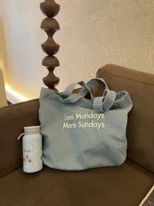 Lifestyle detail of a vintage denim tote bag with 'Less Mondays More Sundays' embroidery