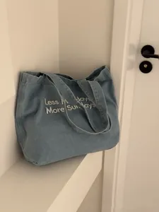 Close-up of a light blue denim tote bag featuring the Less Mondays More Sundays slogan