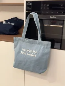 Close-up of denim tote bag with Less Mondays More Sundays white embroidery slogan
