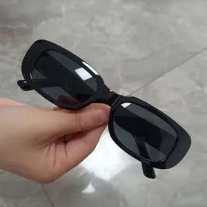Trendy small square black sunglasses held by hand for detailed product display.