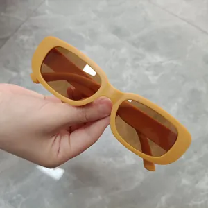 Detailed view of trendy small rectangular yellow sunglasses with brown lenses held in hand.